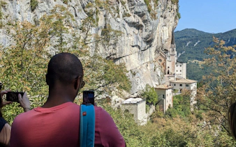 Visitors photographing Madonna della Corona Sanctuary nestled in cliffs, Italy.