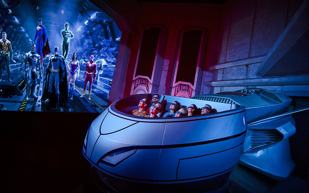 Visitors on a ride at Warner Bros. World Abu Dhabi with superhero figures in the background.
