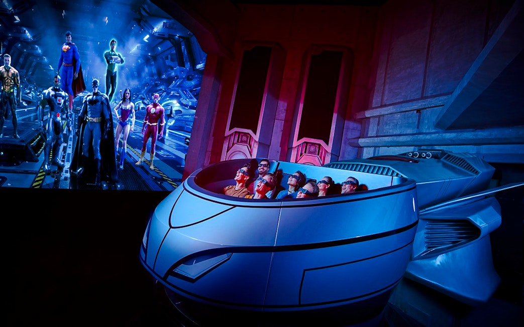 Visitors on a ride at Warner Bros. World Abu Dhabi with superhero figures in the background.