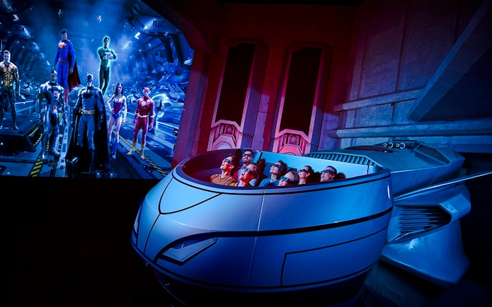 Visitors on a ride at Warner Bros. World Abu Dhabi with superhero figures in the background.