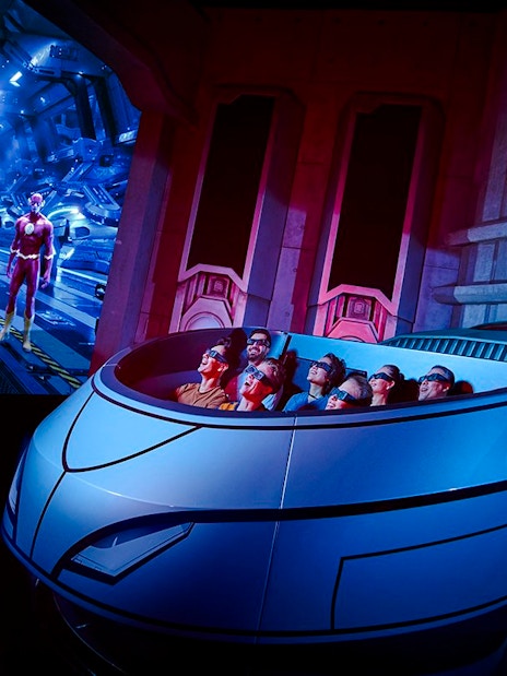 Visitors on a ride at Warner Bros. World Abu Dhabi with superhero figures in the background.