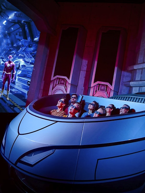 Visitors on a ride at Warner Bros. World Abu Dhabi with superhero figures in the background.
