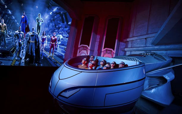 Visitors on a ride at Warner Bros. World Abu Dhabi with superhero figures in the background.