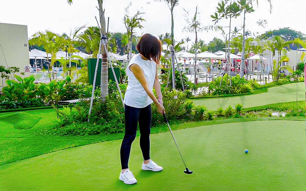 Person playing mini-golf on a lush green course at UltraGolf.