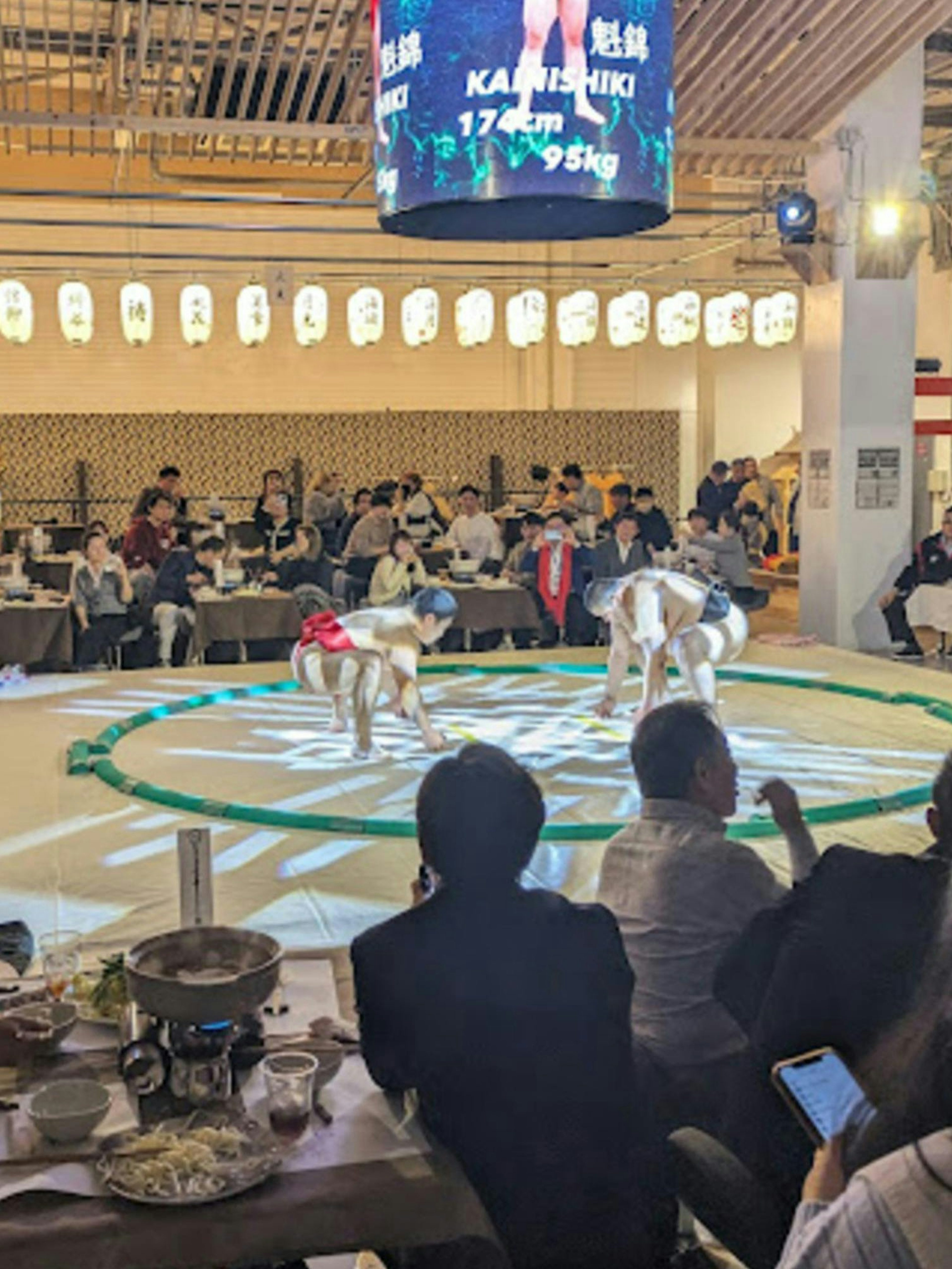 Sumo wrestlers practicing at Ochiizumibeya with audience dining on Chanko-Nabe hot pot.