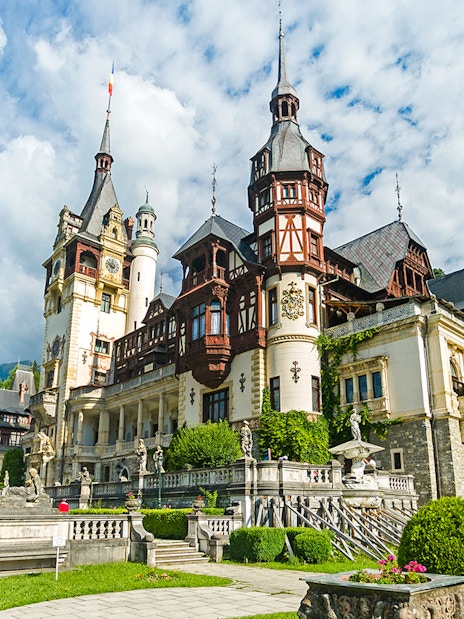 Peles Castle exterior with ornate architecture and surrounding gardens in Sinaia, Romania.