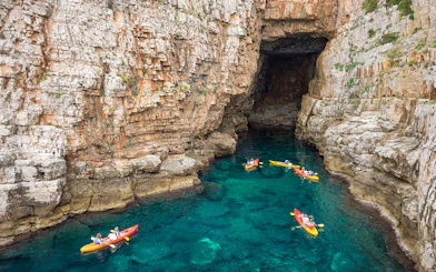 Kayakers exploring sea cave near rocky cliffs in Dubrovnik.