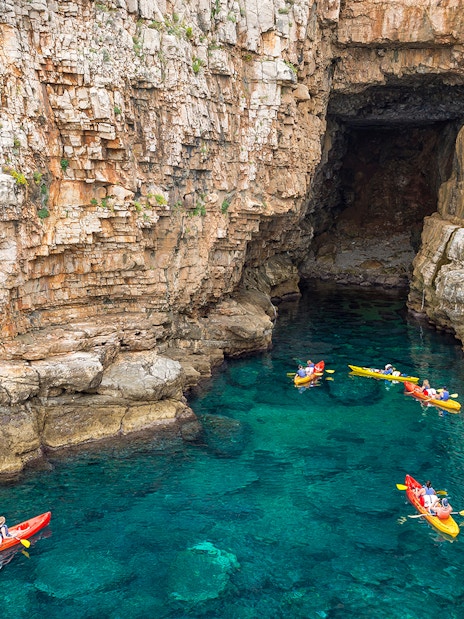 Kayakers exploring sea cave near rocky cliffs in Dubrovnik.