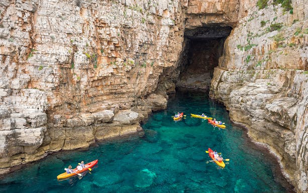 Kayakers paddling near Dubrovnik's historic city walls in the Adriatic Sea.