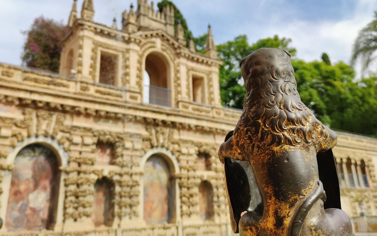Lion statue in front of the Alcázar's ornate facade, Seville, Spain.