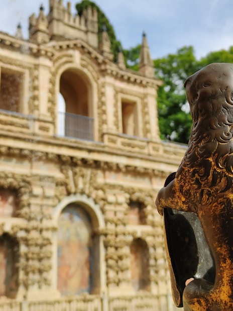 Lion statue in front of the Alcázar's ornate facade, Seville, Spain.