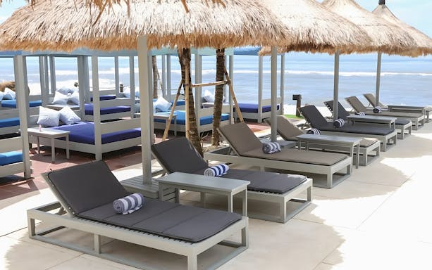 Sun beds under thatched umbrellas at Flamingo Beach Club by the ocean.