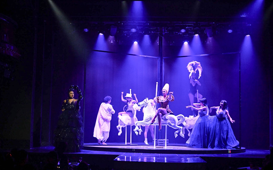 Cabaret performers on stage with carousel horses in Paris show.