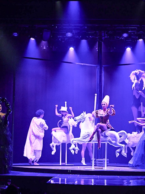 Cabaret performers on stage with carousel horses in Paris show.