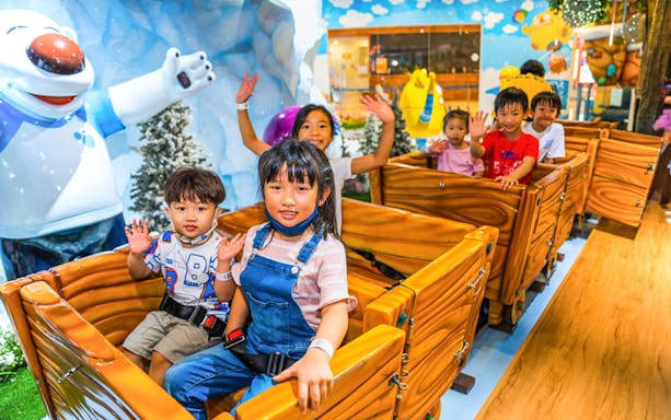 Children enjoying a ride at Pororo Park Singapore with a polar bear statue in the background.
