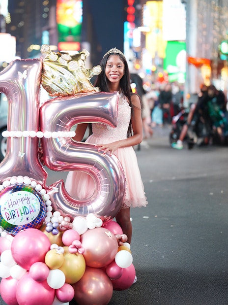 Birthday girl with balloons celebrating sweet 16 in Times Square, NYC.