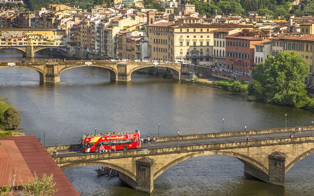 Florence hop-on hop-off tour bus crossing Ponte Vecchio bridge over the Arno River.