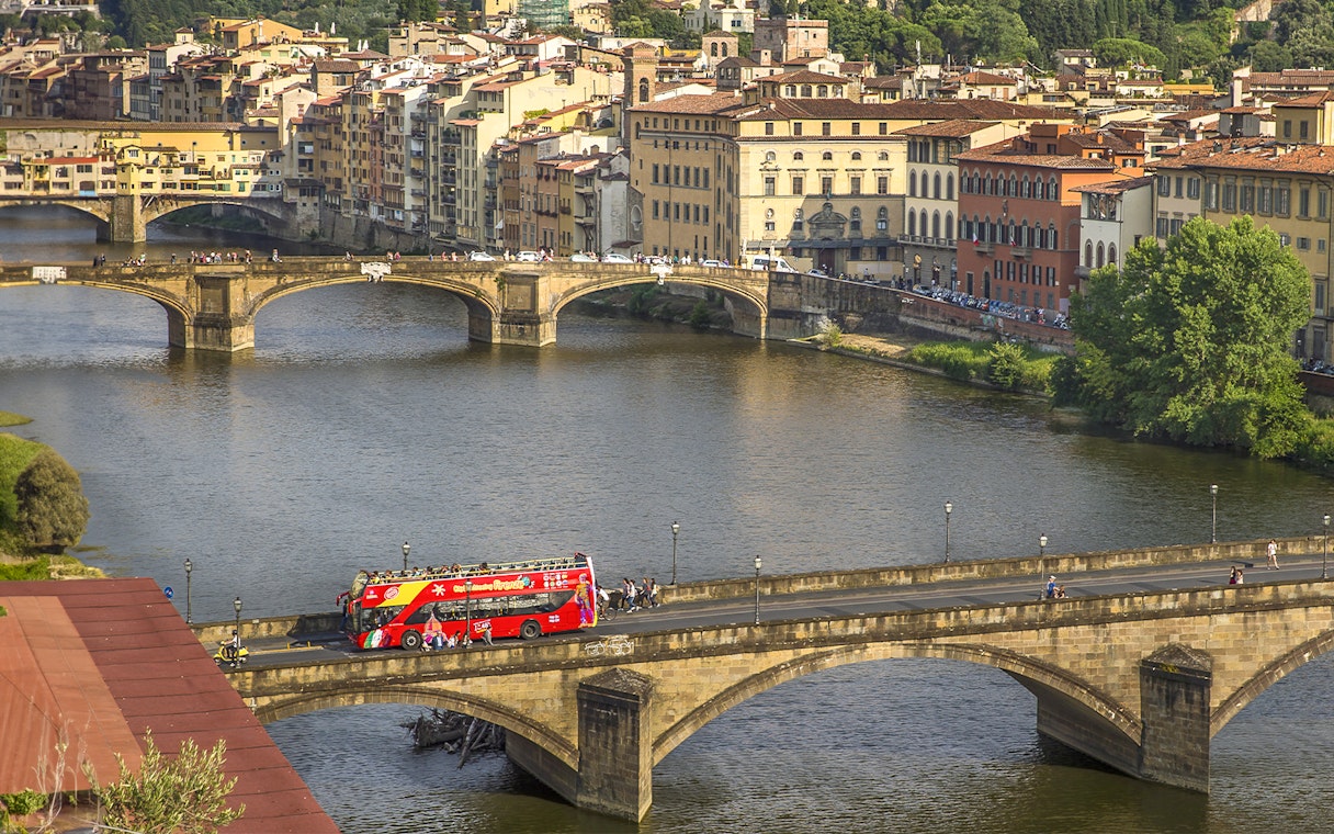 Florence hop-on hop-off tour bus crossing Ponte Vecchio bridge over the Arno River.