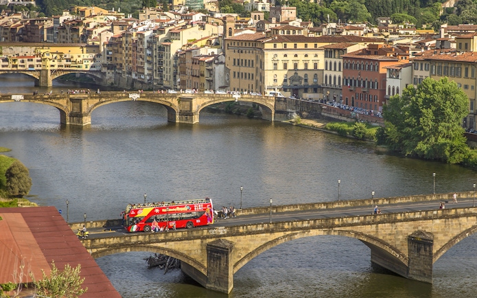 Florence hop-on hop-off tour bus crossing Ponte Vecchio bridge over the Arno River.
