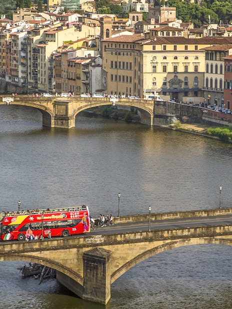 Florence hop-on hop-off tour bus crossing Ponte Vecchio bridge over the Arno River.