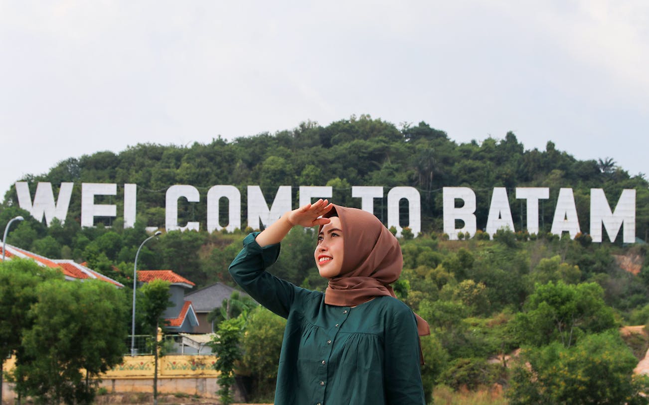 Woman in front of "Welcome to Batam" sign, Batam Day Tour.