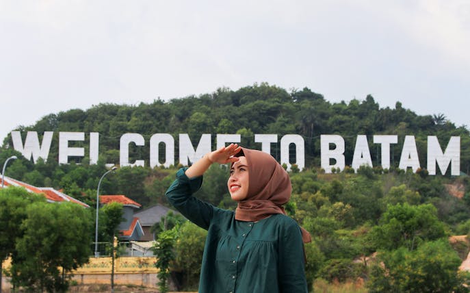 Woman in front of "Welcome to Batam" sign, Batam Day Tour.