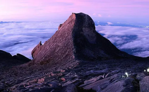 Mountain peak at sunrise with clouds below, viewed from a hiking trail in Dubai.