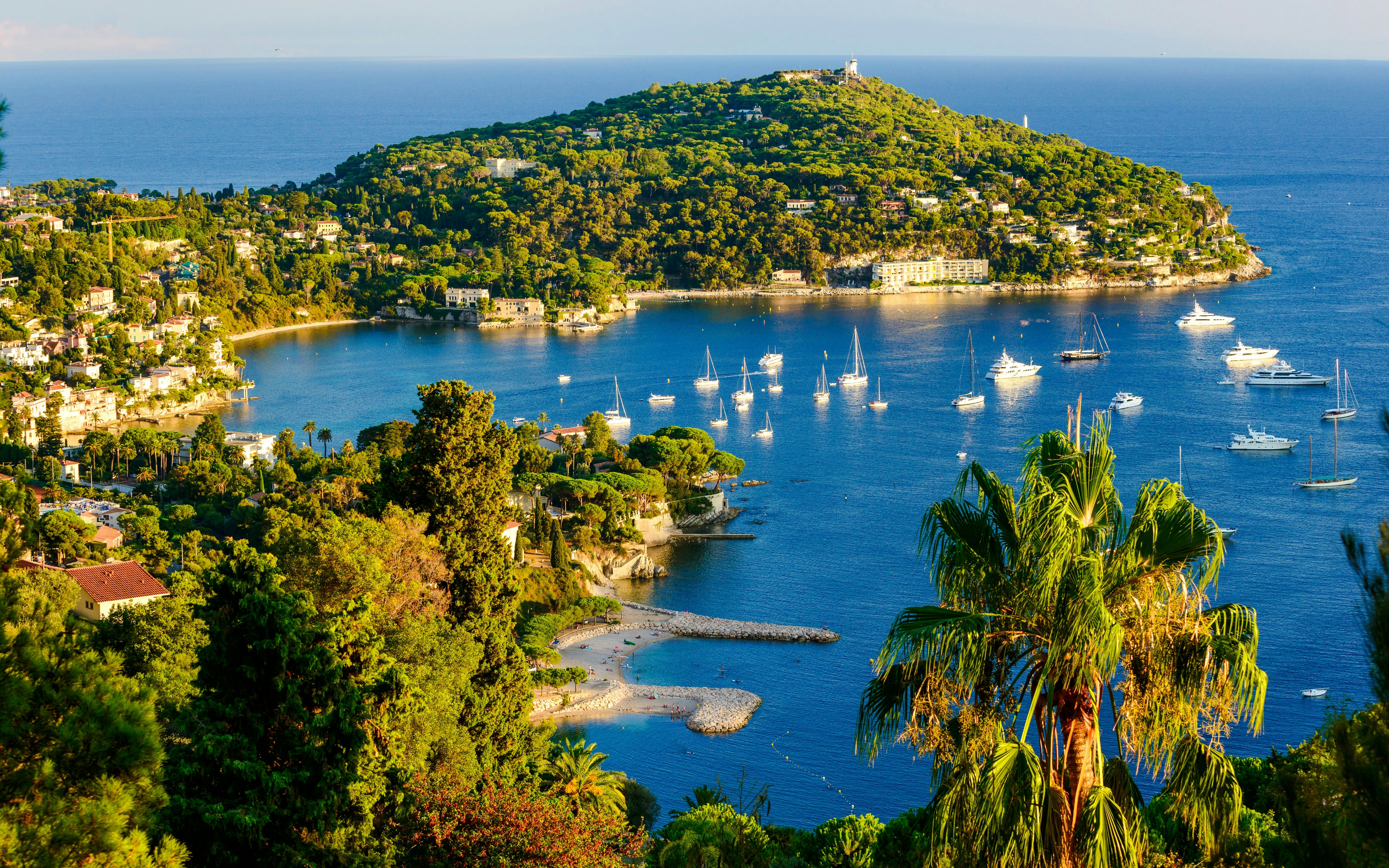 Sailboats in the bay of Cap Ferrat with lush greenery and coastal views.