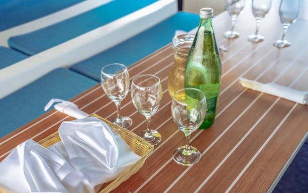 Glasses and bottled drinks on a wooden table aboard a boat.