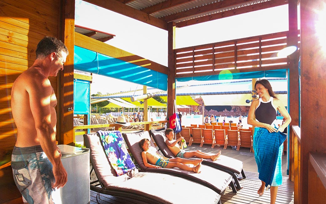 Family relaxing in a cabana at Whitewater World, with children on lounge chairs.
