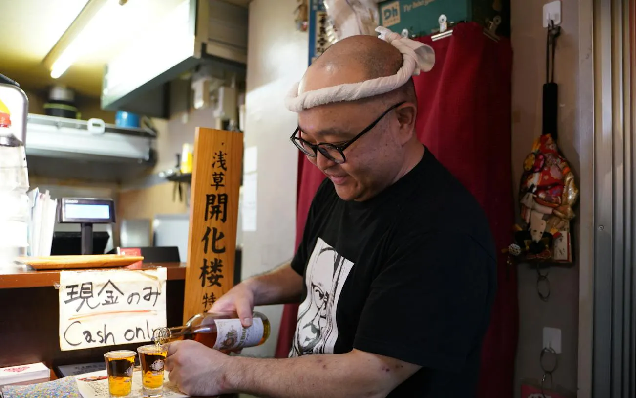 Man pouring drinks at a bar in Asakusa, Tokyo during a night walk tour.
