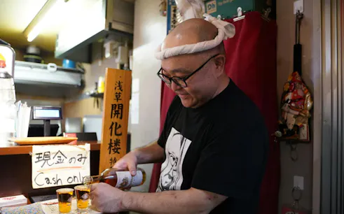 Man pouring drinks at a bar in Asakusa, Tokyo during a night walk tour.