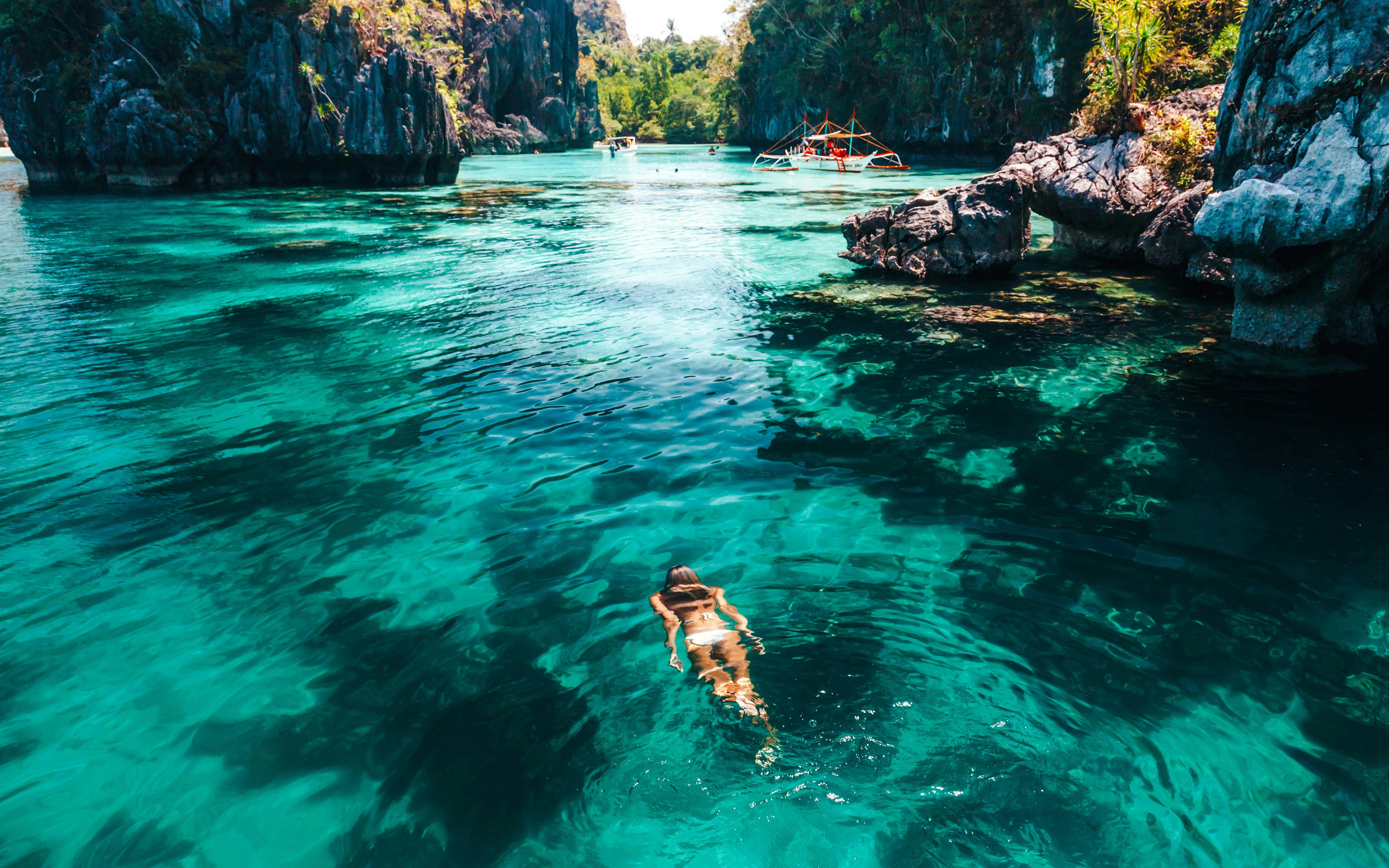 Woman swimming in clear turquoise sea near rocky cliffs in tropical location.