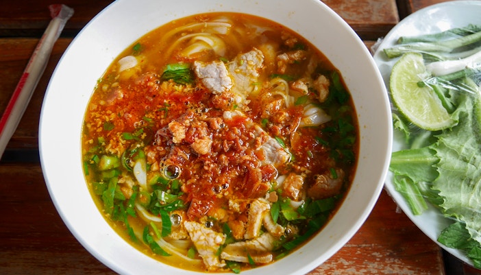Bowl of spicy noodle soup with herbs at a top