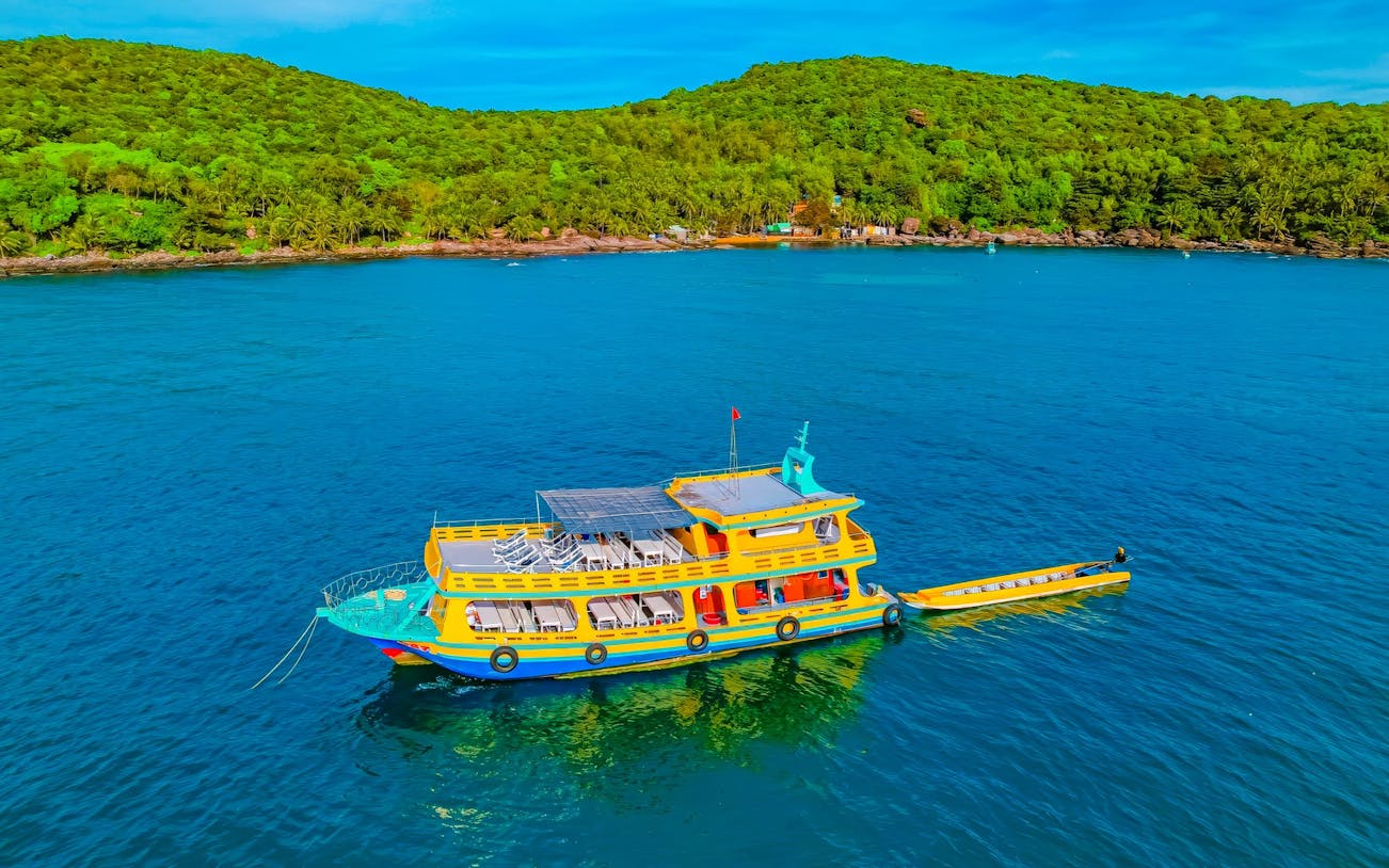 Boat on Phu Quoc 3-island tour with lush green hills in background.