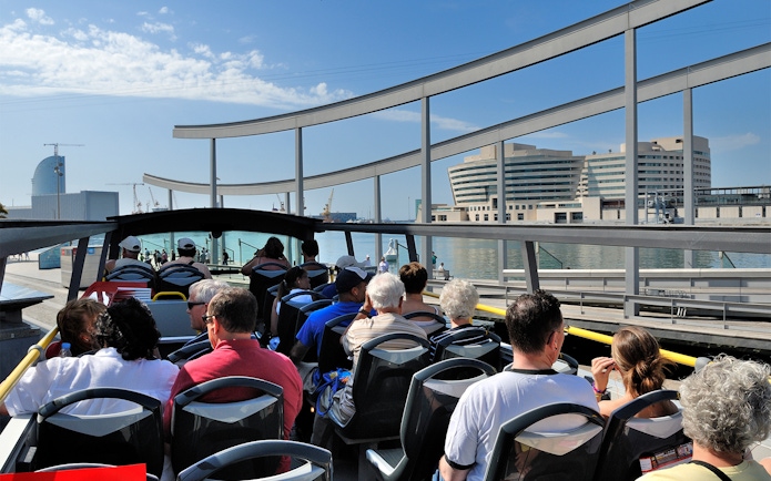 Passengers on Barcelona City Hop On Hop Off Tour bus near waterfront.