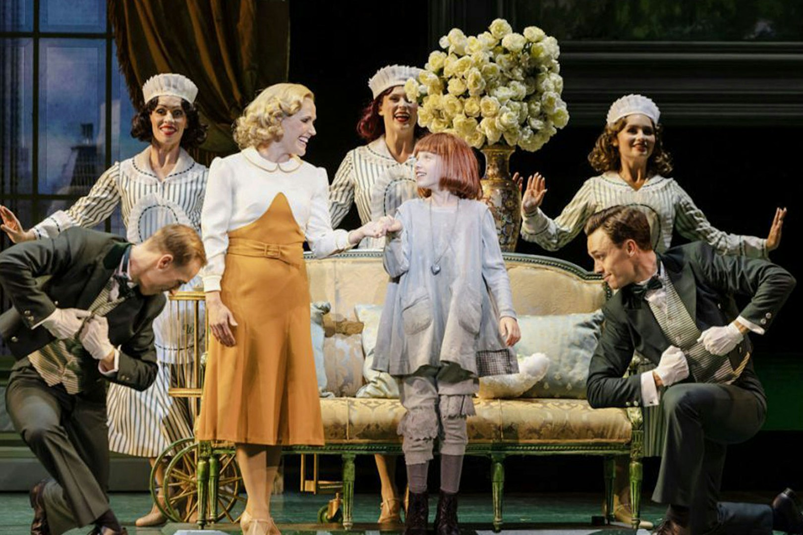 Annie musical scene with characters on stage, featuring a young girl and adults in period costumes.