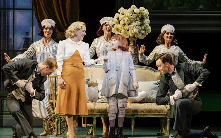 Annie musical scene with characters on stage, featuring a young girl and adults in period costumes.