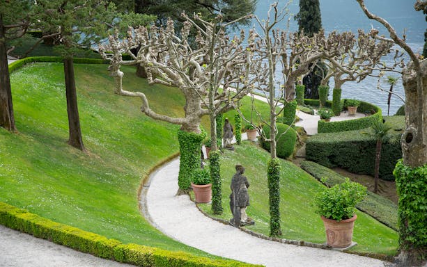 Villa Del Balbianello park path with statues and manicured trees by Lake Como.