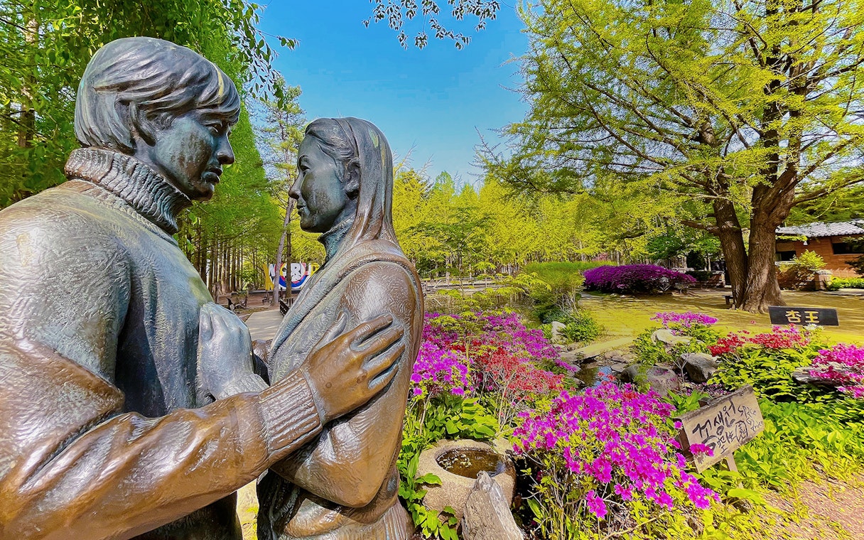 Statue of a couple surrounded by colorful flowers and trees on Nami Island, South Korea.