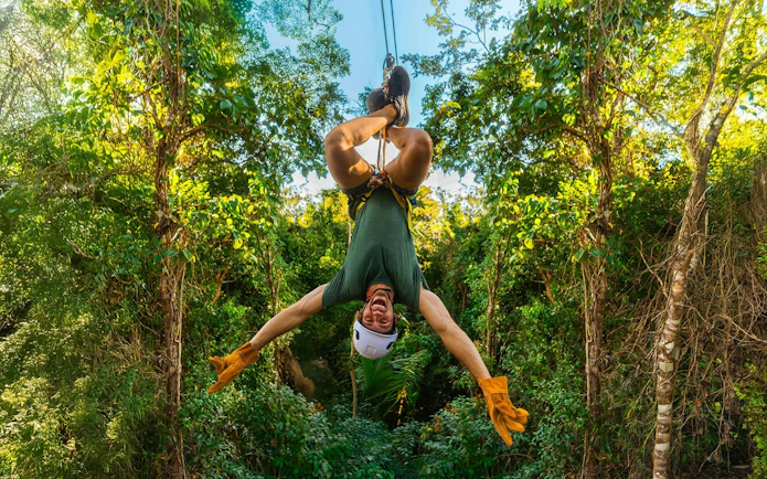 Person ziplining upside down through lush forest at Cancun Extreme Adventuring Park.
