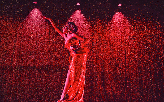 Performer in a sparkling red dress on stage at Paradis Latin festive show.