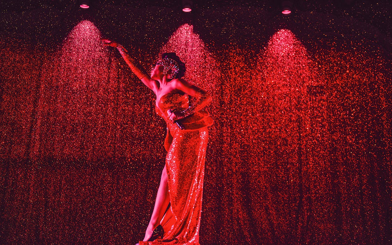 Performer in a sparkling red dress on stage at Paradis Latin festive show.