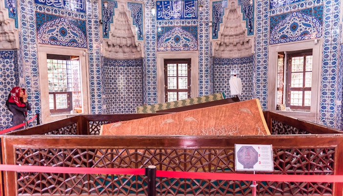Tomb inside Suleymaniye Mosque with intricate blue tilework and a visitor.