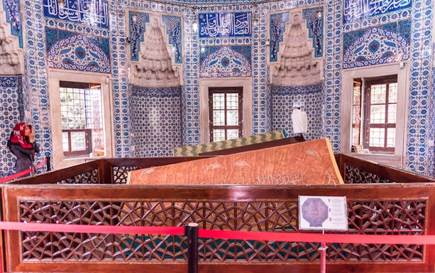 Tomb inside Suleymaniye Mosque with intricate blue tilework and a visitor.