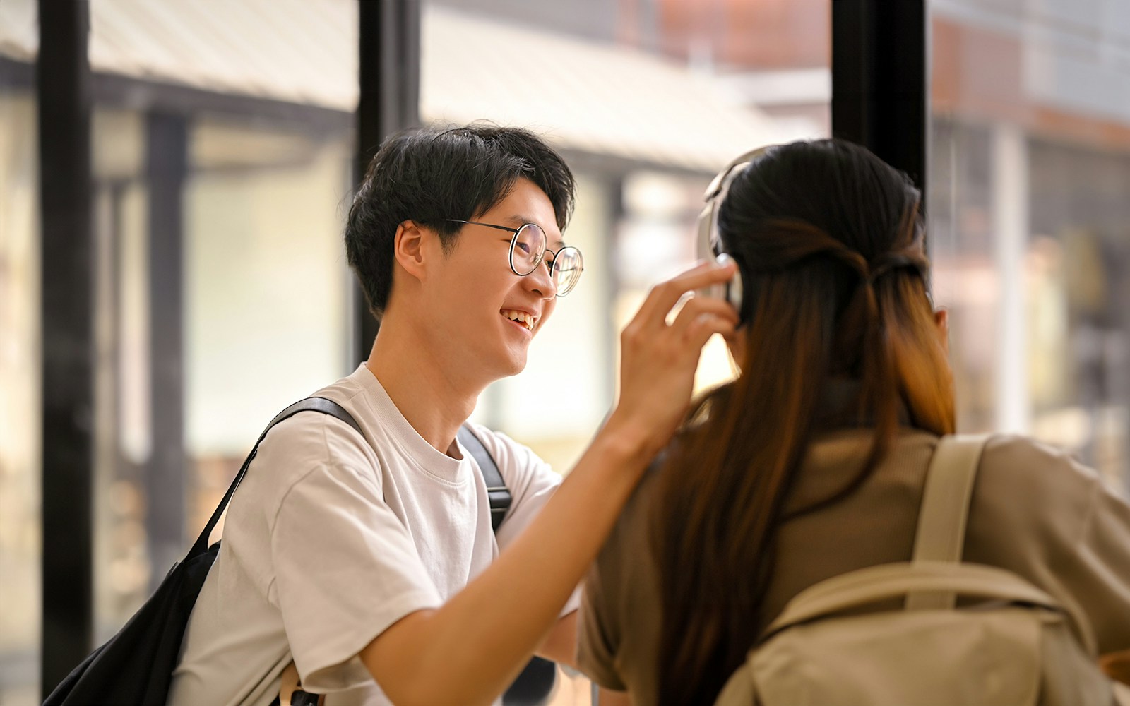 Man placing headphones on woman in a bright indoor setting.