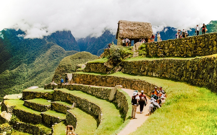 Tourists exploring terraces and stone structures at Machu Picchu, Peru.