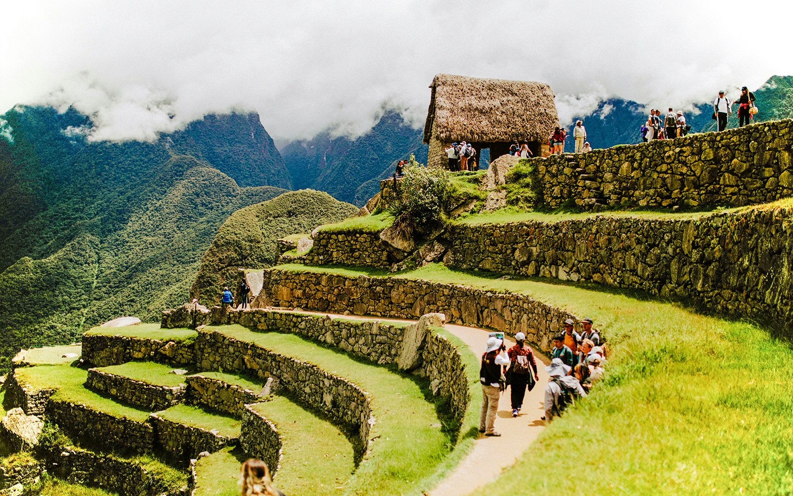 Tourists exploring terraces and stone structures at Machu Picchu, Peru.