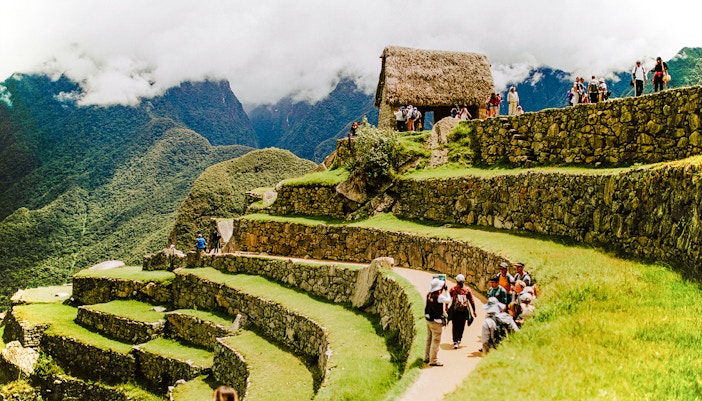 Tourists exploring terraces and stone structures at Machu Picchu, Peru.