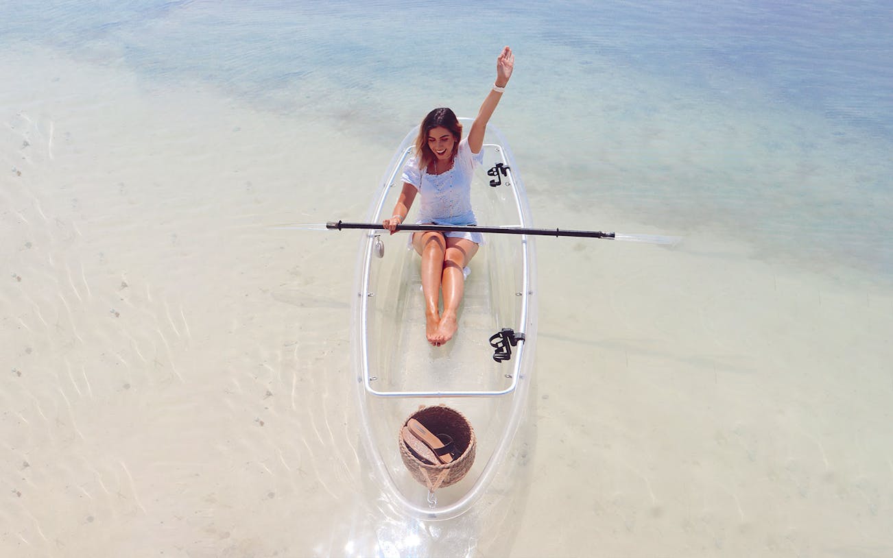 Clear kayak on calm water with person paddling, Burj Khalifa view in Dubai.